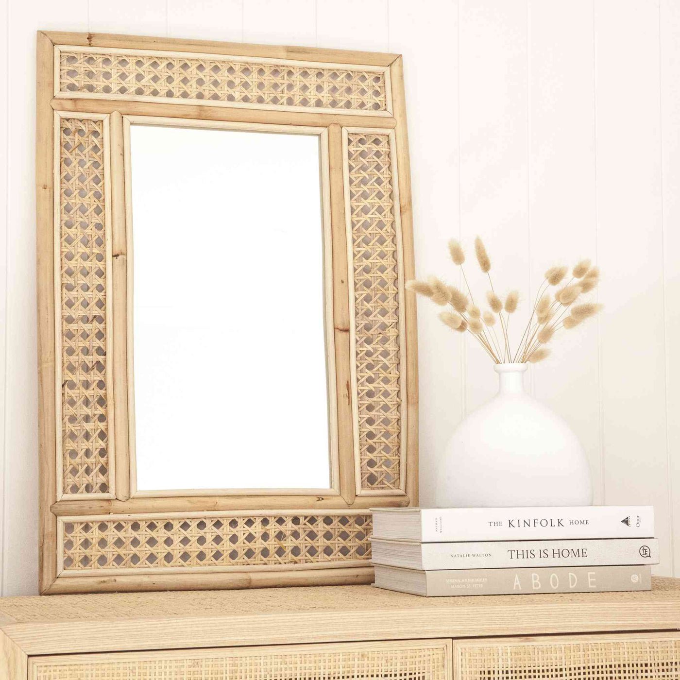 Classic style rentangular rattan mirror with woven rattan frame styled with books on a rattan cupboard..